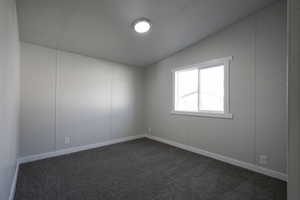 Carpeted empty room featuring vaulted ceiling