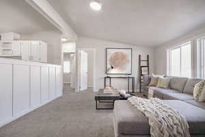 Living room featuring a textured ceiling, light colored carpet, and vaulted ceiling