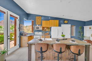 Kitchen with a center island with sink, lofted ceiling, white appliances, and sink