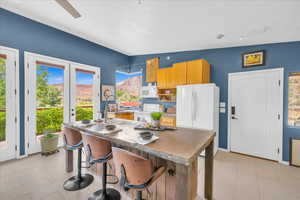 Kitchen with ceiling fan, sink, a kitchen breakfast bar, vaulted ceiling, and white appliances