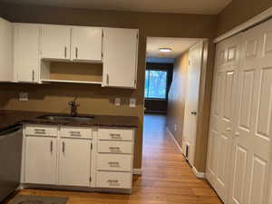 Kitchen featuring sink, light laminate flooring, stainless steel dishwasher, dark stone counters, and white cabinets