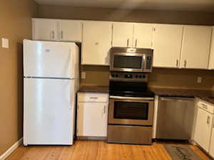 Kitchen featuring white cabinetry, stainless steel appliances, and light laminate flooring