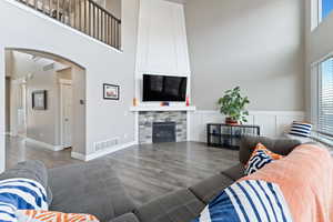 Living room with a stone fireplace, wood-type flooring, and a high ceiling