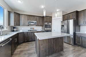 Kitchen with sink, pendant lighting, dark brown cabinets, a kitchen island, and appliances with stainless steel finishes