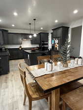 Kitchen with double oven, stainless steel fridge, pendant lighting, a kitchen bar, and light wood-type flooring