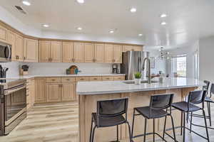 Kitchen with a center island with sink, sink, appliances with stainless steel finishes, a notable chandelier, and light hardwood / wood-style floors