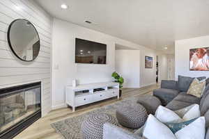 Living room featuring light wood-type flooring, a textured ceiling, and a large fireplace