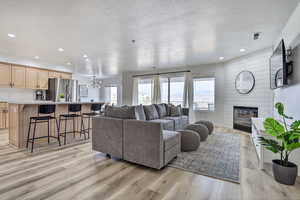 Living room with a fireplace, light wood-type flooring, a textured ceiling, and an inviting chandelier