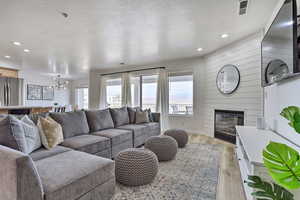 Living room featuring a large fireplace, light wood-type flooring, a textured ceiling, and a chandelier