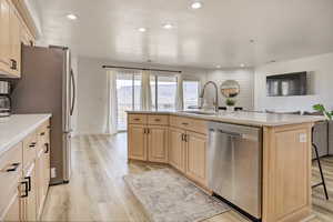 Kitchen with sink, light brown cabinets, stainless steel appliances, light hardwood / wood-style flooring, and a kitchen island with sink