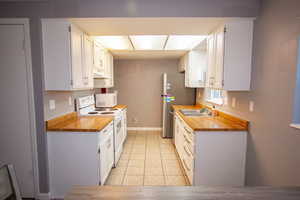 Kitchen featuring white appliances, sink, light tile patterned floors, white cabinetry, and butcher block counters