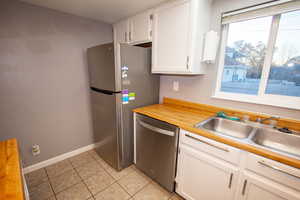 Kitchen with light tile patterned flooring, sink, white cabinets, and stainless steel appliances