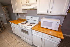 Kitchen with white cabinets, white appliances, butcher block countertops, and light tile patterned flooring