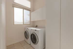 Washroom featuring cabinets, light tile patterned floors, and washing machine and clothes dryer