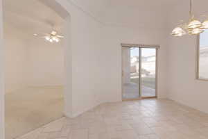 Empty room featuring ceiling fan with notable chandelier, light colored carpet, and ornamental molding