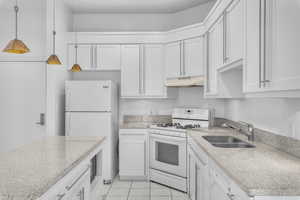 Kitchen with white appliances, white cabinets, sink, hanging light fixtures, and light tile patterned flooring