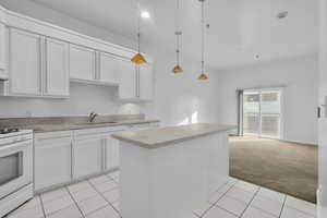 Kitchen featuring white stove, white cabinets, sink, hanging light fixtures, and light colored carpet