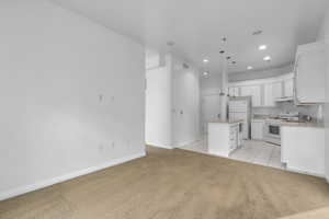 Kitchen featuring hanging light fixtures, white cabinets, light colored carpet, and white appliances