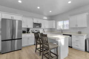 Kitchen featuring white cabinetry, sink, a breakfast bar, a kitchen island, and appliances with stainless steel finishes