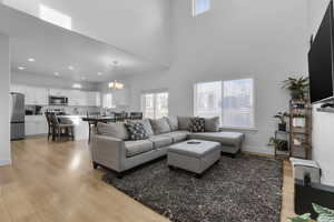 Living room with light wood-type flooring, a towering ceiling, and a chandelier