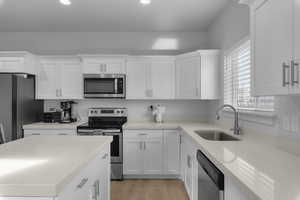 Kitchen featuring appliances with stainless steel finishes, light wood-type flooring, white cabinetry, and sink