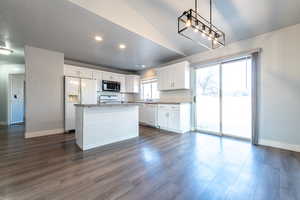 Kitchen with backsplash, white appliances, vaulted ceiling, white cabinets, and a center island