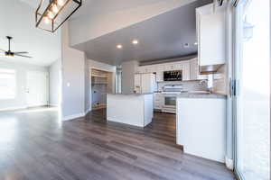 Kitchen with white appliances, ceiling fan, white cabinets, a kitchen island, and lofted ceiling