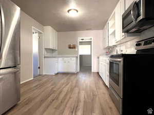 Kitchen featuring a textured ceiling, stainless steel appliances, white cabinetry, and light hardwood / wood-style flooring