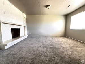 Unfurnished living room featuring carpet flooring, a large fireplace, and a textured ceiling