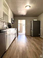 Kitchen featuring white cabinetry, sink, stainless steel appliances, light hardwood / wood-style flooring, and a textured ceiling