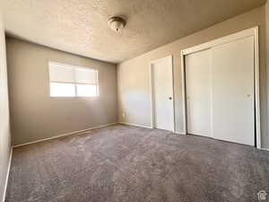 Unfurnished bedroom with dark carpet, a textured ceiling, and a closet