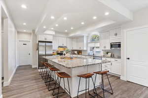 Kitchen with a kitchen bar, light stone countertops, stainless steel appliances, white cabinets, and a kitchen island