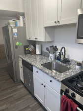 Kitchen featuring light stone countertops, white cabinetry, sink, stainless steel appliances, and dark hardwood / wood-style flooring