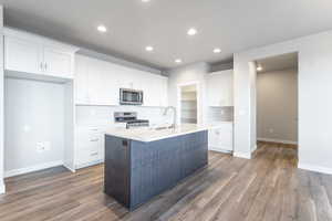 Kitchen with white cabinetry, sink, a center island with sink, appliances with stainless steel finishes, and hardwood / wood-style flooring