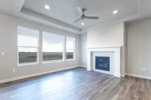 Unfurnished living room with hardwood / wood-style floors, a tray ceiling, and ceiling fan