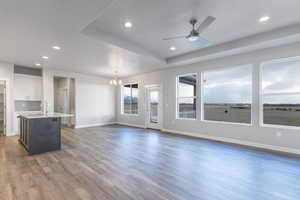 Unfurnished living room featuring a tray ceiling, sink, dark hardwood / wood-style floors, and ceiling fan with notable chandelier