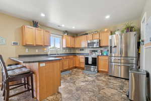 Kitchen featuring a breakfast bar, sink, light brown cabinetry, appliances with stainless steel finishes, and kitchen peninsula