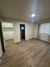 Unfurnished bedroom featuring a walk in closet, light hardwood / wood-style flooring, connected bathroom, and a closet