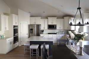 Kitchen featuring a center island, stainless steel appliances, pendant lighting, vaulted ceiling, and white cabinets