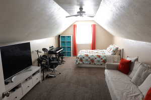 Bedroom with carpet, a textured ceiling, vaulted ceiling, and ceiling fan