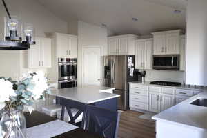 Kitchen featuring white cabinetry, backsplash, appliances with stainless steel finishes, and vaulted ceiling