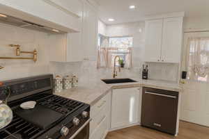 Kitchen featuring white cabinets, appliances with stainless steel finishes, range hood, and sink