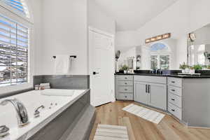 Bathroom with vanity, wood-type flooring, a tub, and vaulted ceiling