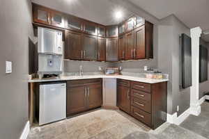 Wet bar with dark brown cabinets, light stone countertops, sink, and stainless steel mini refrigerator