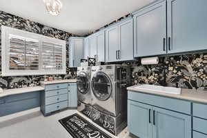 Laundry room with washer and dryer, sink, cabinets, and wall papered walls