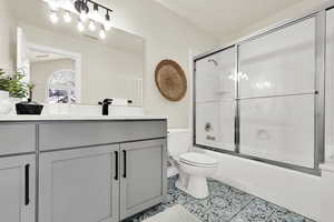 Full bathroom with tile patterned floors, vanity, enclosed tub / shower combo, and toilet