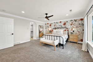 Carpeted bedroom featuring ceiling fan, crown molding, and wall papered feature wall