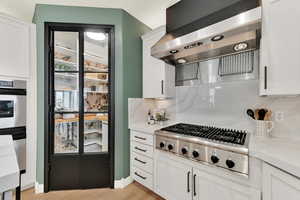 Kitchen featuring light grey cabinetry, quartz backsplash, exhaust hood, and appliances with stainless steel finishes