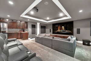 Carpeted home theater featuring a raised ceiling and wet bar