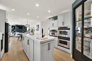 Kitchen featuring a center island with sink, light grey cabinets, light hardwood / wood-style floors, and stainless steel double oven